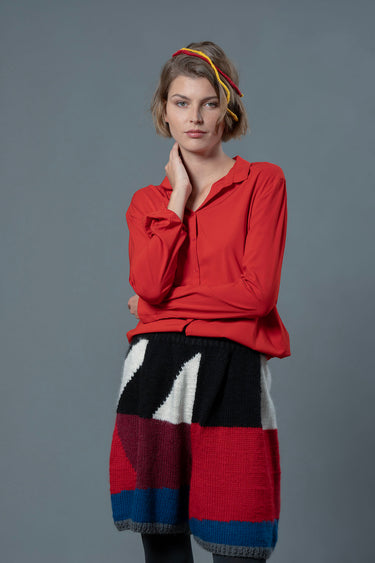 woman wearing red button up shirt and wool bermuda shorts with black, white, bordeau, red and blue colour block patterns.
